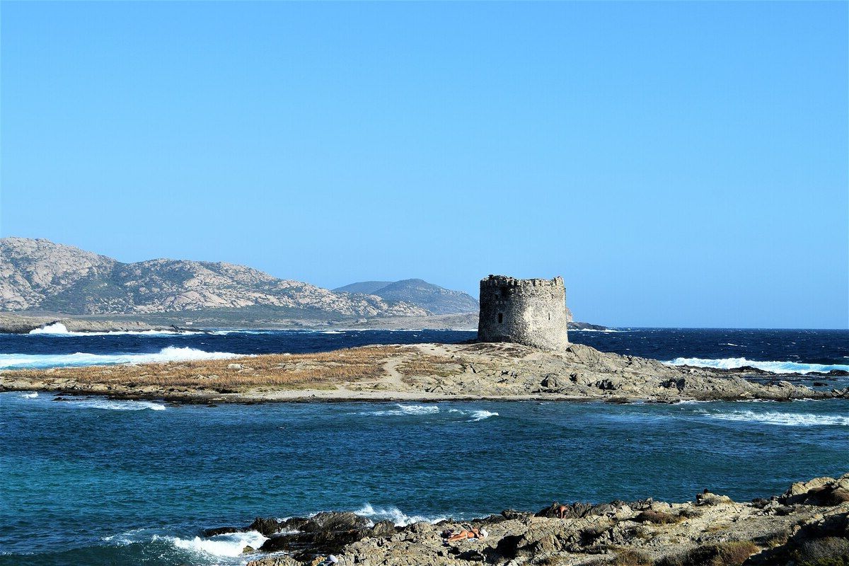 Scorcio ravvicinato della Torre della Pelosa con mare cristallino sullo sfondo, una barca di pescatori in primo piano
