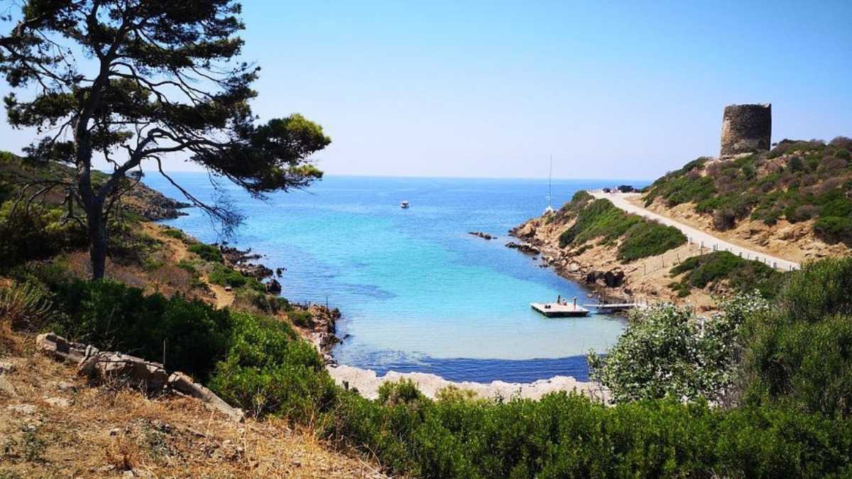Vista panoramica della spiaggia La Pelosa con il mare turchese, sabbia bianca e la torre aragonese sullo sfondo. Barche ormeggiate nelle acque limpide di Stintino.