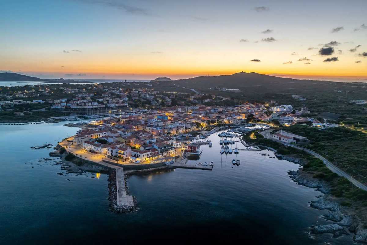 Panorama del porto vecchio di Stintino durante una festa locale, decorazioni tradizionali e folla festante, atmosfera serale vivace